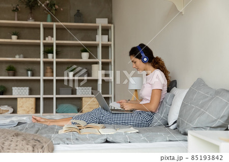 Woman in headphones using laptop, studying online, sitting on bed 85193842