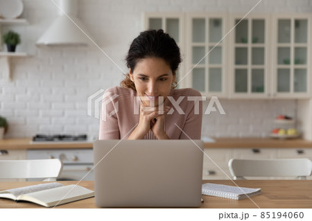 Smiling woman looking at laptop screen, working online in kitchen 85194060
