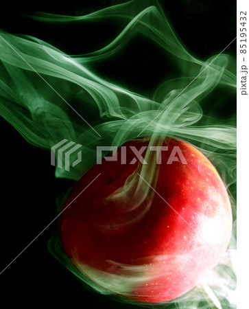 Green smoke envelops a round red apple on a black background 85195432