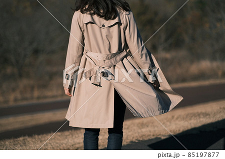 風になびくトレンチコートを着た女性の後ろ姿　 85197877