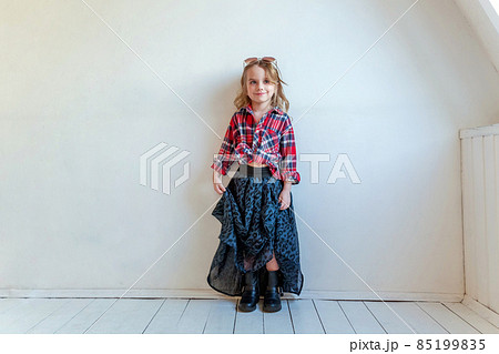 Sweet happy adorable fashion young little girl dressed like hipster hippie gipsy cowboy in sunglasses standing against white wall background in light bright room. Lifestyle people trendy concept 85199835