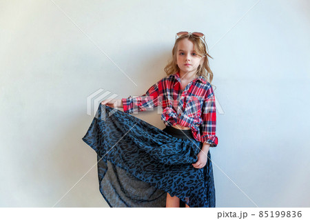 Sweet happy adorable fashion young little girl dressed like hipster hippie gipsy cowboy in sunglasses standing against white wall background in light bright room. Lifestyle people trendy concept 85199836