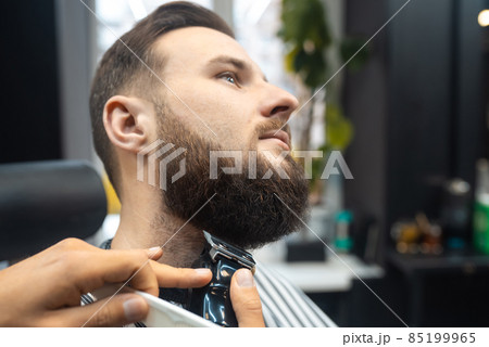 Barber works with a beard clipper. Hipster client getting haircut. 85199965