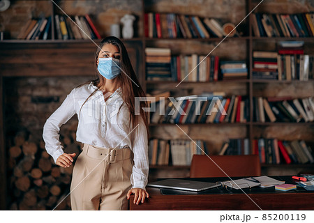 Young woman in medical face mask at home on bookshelves background Young woman in medical face mask at home on bookshelves background 85200119