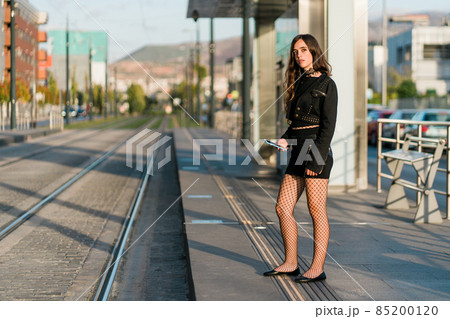 young woman waiting for the tram at the stop young woman waiting for the tram at the stop 85200120