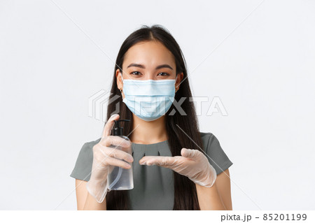 Small business owners, covid-19, preventing virus measures concept. Close-up of smiling asian woman in medical mask and gloves desinfecting it with hand sanitizer before packing customer order Small business owners, covid-19, preventing virus measures concept. Close-up of smiling asian woman in medical mask and gloves desinfecting it with hand sanitizer before packing customer order 85201199