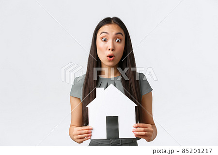 Insurance, loan, real estate and family concept. Surprised asian woman in dress, holding paper house in hands react to big announcement, found excellent apartment for cheap price, white background 85201217
