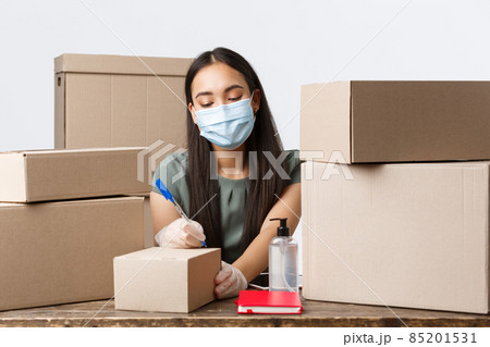 Small business owners, e-commerce and covid-19 preventing virus concept. Asian businesswoman in medical mask and gloves, using hand sanitizer while processing order, packing client boxes Small business owners, e-commerce and covid-19 preventing virus concept. Asian businesswoman in medical mask and gloves, using hand sanitizer while processing order, packing client boxes 85201531