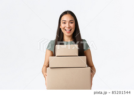Small business owners, startup and work from home concept. Cheerful asian female store manager carry boxes with clients orders at post office, making delivery of purchased iteam, white background 85201544