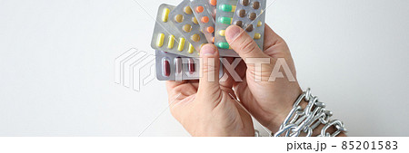 Male hands tied with chain and hold various medical pills closeup 85201583