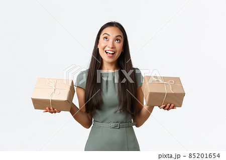 Happy dreamy asian female entrepreneur, small business owner packing items herself, sending packages to customers who ordered products online store, standing white background and looking up 85201654