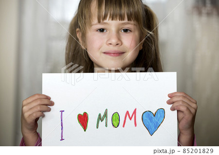 Cute child girl wit sheet of paper with colorful crayons painted words I love Mom. Art education, creativity concept. Cute child girl wit sheet of paper with colorful crayons painted words I love Mom. Art education, creativity concept. 85201829