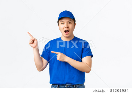 Amazed and impressed asian courier in blue uniform making announcement, gasping amazed and pointing upper left corner at something awesome. Delivery guy demonstrate banner 85201984