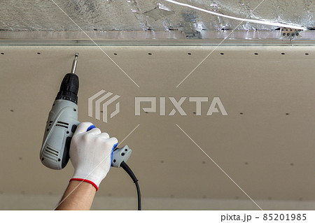 Worker hand with screwdriver connecting suspended drywall ceiling to metal frame. Renovation, construction and DIY concept. 85201985