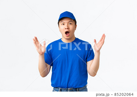 Surprised and excited courier in blue uniform react to awesome news, big announcement in mail company. Impressed delivery guy shaking raised hands and gasping amazed, white background 85202064