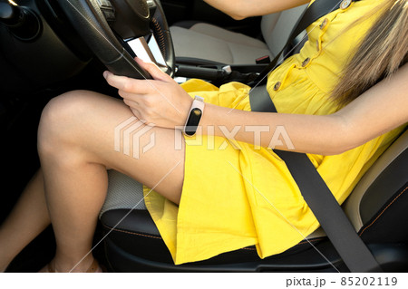 Close up of young woman driver legs in yellow summer dress sitting behind steering wheel driving a car. 85202119