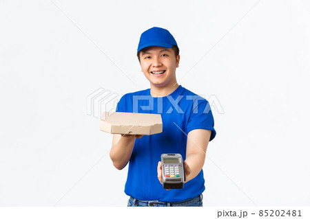 Contactless shopping, payment and delivery concept. Cheerful friendly, smiling asian courier in blue uniform bring order to client home, handing pizza box and POS terminal, white background 85202481
