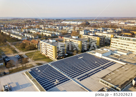 Aerial view of blue shiny solar photo voltaic panels system on commercial roof producing renewable clean energy on city landscape background. 85202623