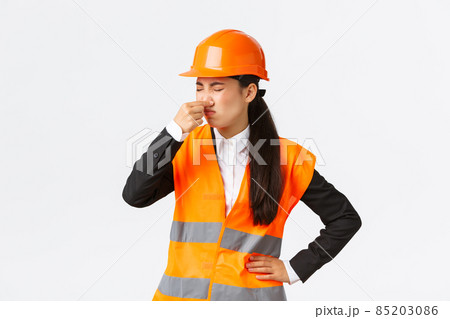 Disgusted and displeased asian female architect enter construction area and shut ears as smell disgusting reek, awful smell, grimacing from discomfort, standing in safety helmet over white background 85203086