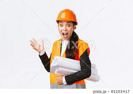 Impressed and fascinated asian female engineer, lead architect at construction area, pointing behind at something awesome, carry blueprint of project, wearing safety helmet and reflective jacket 85203417
