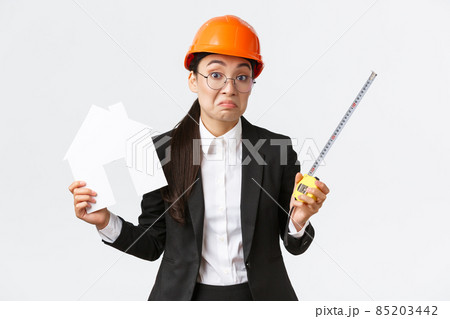 Confused indecisive asian female architect dont know what do, engineer in helmet and business suit shrugging while holding home maket and measuring tape, white background Confused indecisive asian female architect dont know what do, engineer in helmet and business suit shrugging while holding home maket and measuring tape, white background 85203442