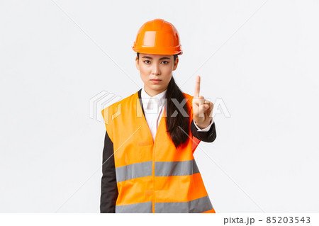 Serious-looking confident and displeased asian female engineer shaking finger, scolding construction worker for acting dangerous, prohibit and forbid action at building zone, white background 85203543