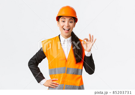 Satisfied happy asian female engineer, construction manager in safety helmet and reflective jacket showing okay gesture pleased, guarantee building quality, ensure everything excellent Satisfied happy asian female engineer, construction manager in safety helmet and reflective jacket showing okay gesture pleased, guarantee building quality, ensure everything excellent 85203731