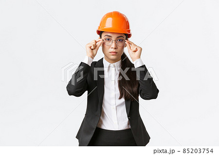 Lets get to business. Serious-looking confident female asian chief engineer inspect enterprise, wearing safety helmet and suit, put on glasses, standing white background, ready to work Lets get to business. Serious-looking confident female asian chief engineer inspect enterprise, wearing safety helmet and suit, put on glasses, standing white background, ready to work 85203754