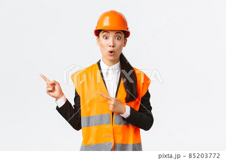 Building, construction and industrial concept. Surprised and impressed asian female chief engineer pointing upper left corner. Estate agent showing way, discuss interesting project, white background Building, construction and industrial concept. Surprised and impressed asian female chief engineer pointing upper left corner. Estate agent showing way, discuss interesting project, white background 85203772