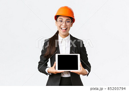 Excited and amazed smiling asian female construction engineer, architect in safety helmet and business suit, showing digital tablet screen with amazed expression, standing white background Excited and amazed smiling asian female construction engineer, architect in safety helmet and business suit, showing digital tablet screen with amazed expression, standing white background 85203794