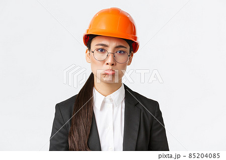 Close-up of upset and gloomy asian female construction manager facing failure, bad results on factory, engineer standing in safety helmet and business suit pouting sad, standing white background Close-up of upset and gloomy asian female construction manager facing failure, bad results on factory, engineer standing in safety helmet and business suit pouting sad, standing white background 85204085