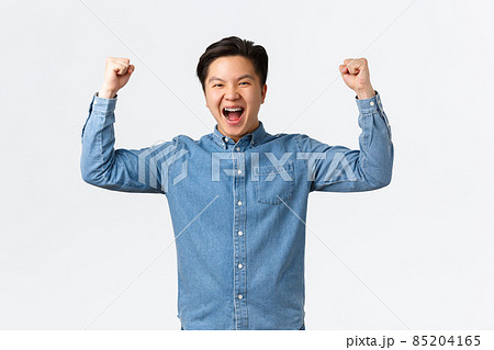 Excited happy asian man with braces feeling success over winning prize, fist pump and shouting yes, rejoicing, triumphing as becoming champion, standing white background celebrating 85204165