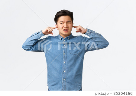 Disturbed and frustrated asian man complaining loud noise, shut ears and looking left displeased, frowning upset, telling neighbour be quiet, college student cant focus because of noisy awful music 85204166