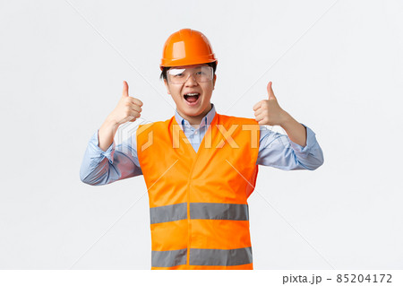 Building sector and industrial workers concept. Smiling asian male engineer, architect or builder in safety helmet and reflective clothing showing thumbs-up, assure everything alright Building sector and industrial workers concept. Smiling asian male engineer, architect or builder in safety helmet and reflective clothing showing thumbs-up, assure everything alright 85204172