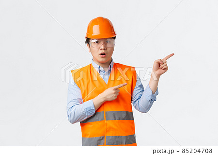 Building sector and industrial workers concept. Impressed and amazed asian construction manager, engineer in helmet and reflective clothing pointing upper right corner, white background Building sector and industrial workers concept. Impressed and amazed asian construction manager, engineer in helmet and reflective clothing pointing upper right corner, white background 85204708