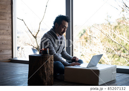 ウッドデッキなどでパソコンを見ながら考えるハンサムなアジア人（日本人）コピースペース　縦 85207132