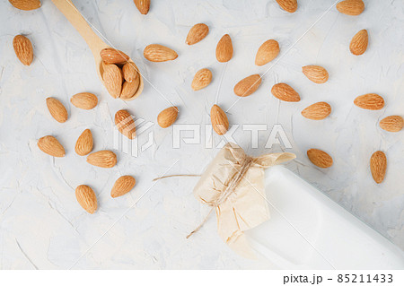 Milk from organic almonds in a transparent bottle with a scattering of seeds and a wooden spoon on a light background 85211433
