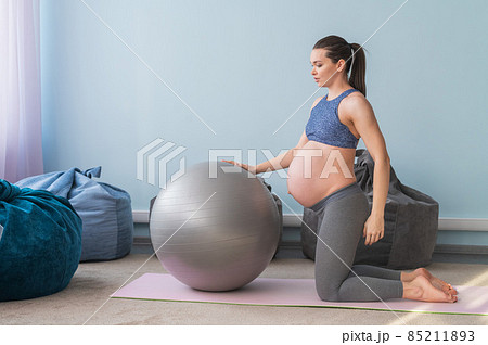 Pregnant european woman performs exercises with fitness ball. Expectant mother is doing yoga in the 3rd trimester. Girl in the classroom in preparation for childbirth. 85211893