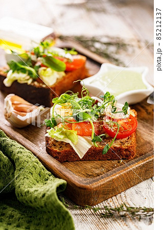 Close-up toast with salted fish, cheese, egg, onion rings and salad. Appetizing canapes or sandwiches with smoked salmon. Traditional Delicious breakfast or snack on a wooden background Vertical shot Close-up toast with salted fish, cheese, egg, onion rings and salad. Appetizing canapes or sandwiches with smoked salmon. Traditional Delicious breakfast or snack on a wooden background Vertical shot 85212137