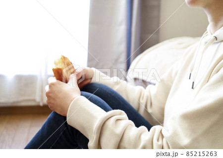 部屋で床に座り込みパンを食べる女性 85215263