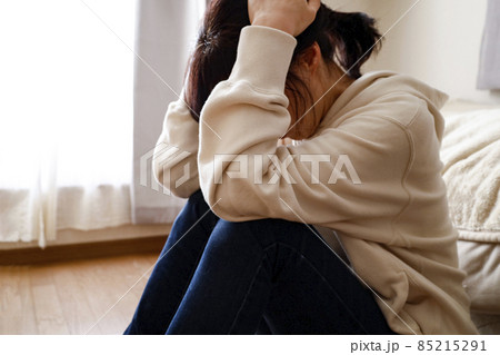部屋で床に座り込み頭を抱える女性 部屋で床に座り込み頭を抱える女性 85215291