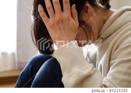 部屋で床に座り込み頭を抱える女性 部屋で床に座り込み頭を抱える女性 85215292