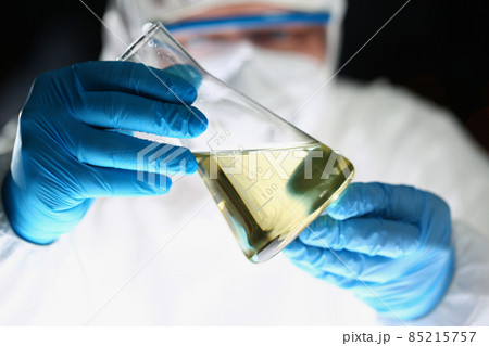 Laboratory pharmacist in respirator and uniform show flask with yellow liquid 85215757