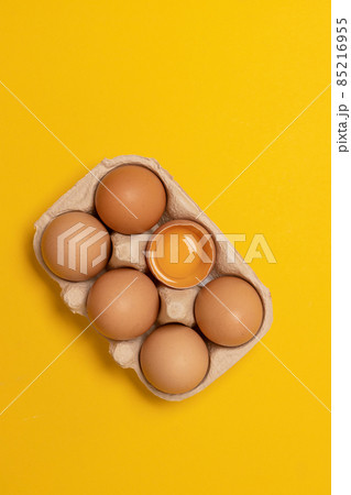 Brown chicken eggs and one broken egg with yolk in eco basket on yellow background 85216955