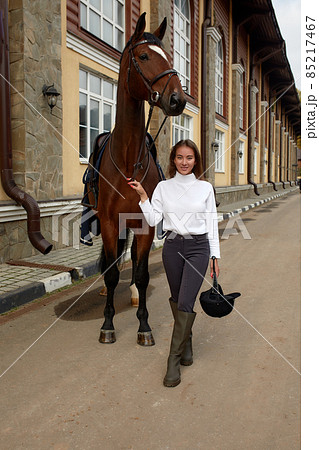 Female horseman going with her brown horse outdoor. Concept of animal care. Rural rest and leisure. Idea of green tourism. Young european woman wearing helmet and uniform 85217467