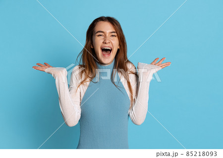 Half-length portrait of pretty girl with long glossy hair spreads her arms to side in delight isolated on blue studio backgroud. 85218093