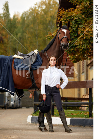 Female horseman going with her brown horse outdoor. Concept of animal care. Rural rest and leisure. Idea of green tourism. Young european woman wearing helmet and uniform 85218384