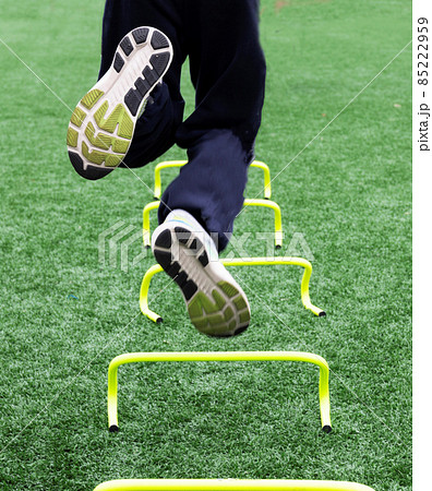 Athlete jumping over small yellow hurdles on one leg close up 85222959