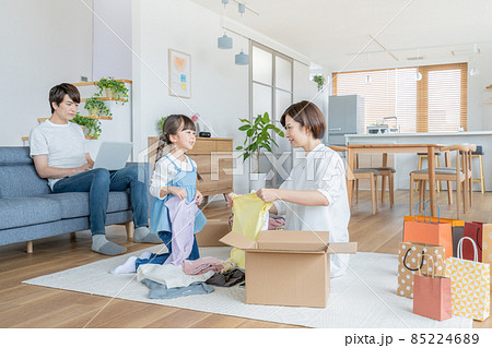 ママと衣類の片付けのお手伝いをする小学生の女の子とソファに座ってパソコン作業をするパパ 85224689