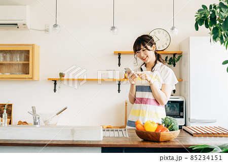 キッチンでスマホを持つ女性(スマホ・笑顔) キッチンでスマホを持つ女性(スマホ・笑顔) 85234151